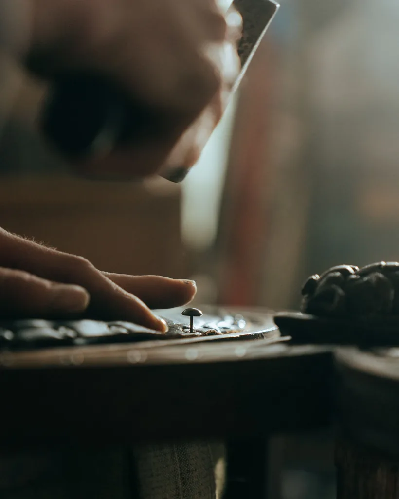 Manos colocando pequeñas tachuelas en el canto de un mueble de madera en un taller con poca luz